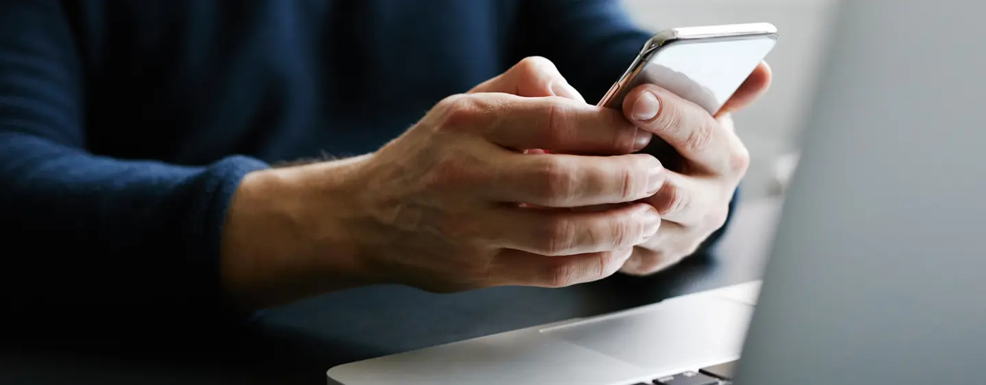 A person sitting at their computer with a phone in their hands