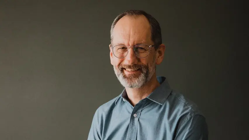 A smiling man in a blue collared shirt and glasses. 