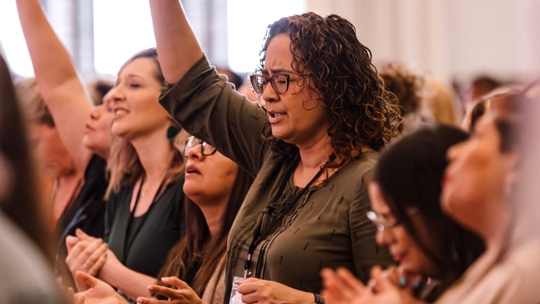 A group of women singing with arms raised