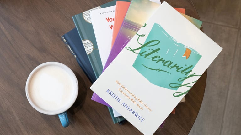 A stack of books and a cup of coffee on a brown table.