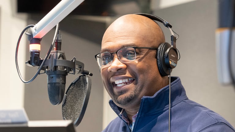 A smiling man wearing headphones in front of a recording microphone.